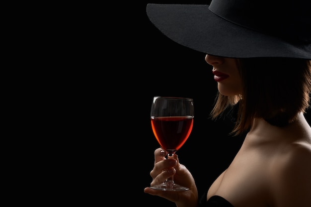 Shot of a sexy woman in a black hat hiding her face drinking wine