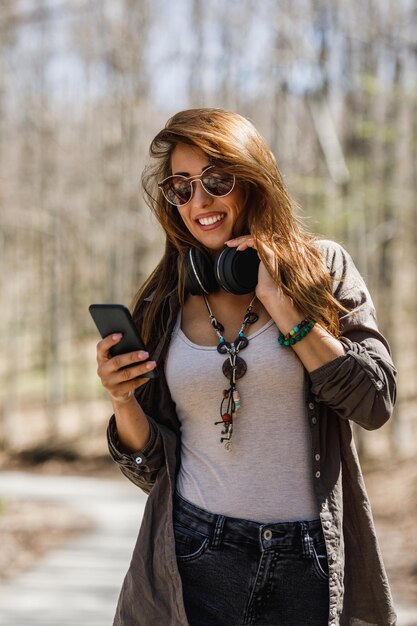 自然の中を歩きながらスマートフォンを使って笑顔の若い女性のショット。