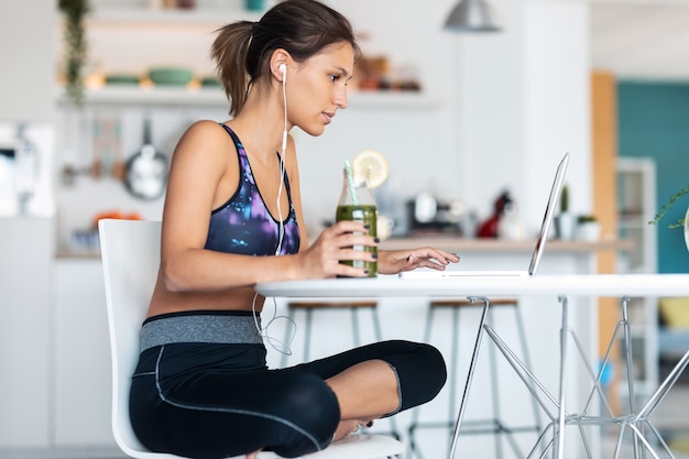 Shot of sporty young woman working with her laptop after session of exercises in the kitchen at home.