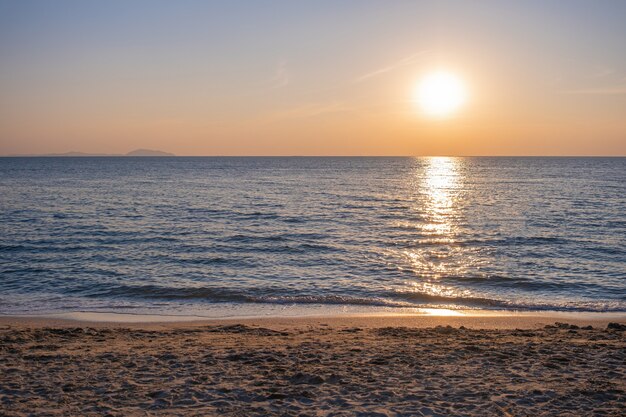 夏の熱帯の砂浜で波と自然の海に沈む夕日のショット