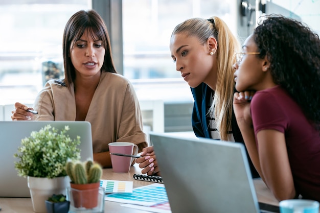 Inquadratura di tre moderne imprenditrici che parlano e rivedono l'ultimo lavoro svolto al computer in uno spazio di lavoro comune