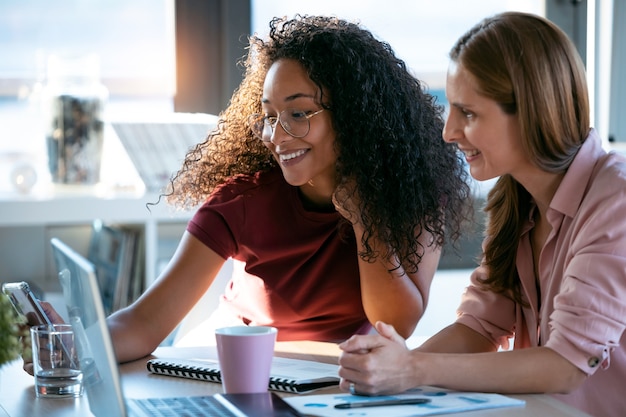 Shot of two beautiful business women working together with laptop while talking about job news in the office.