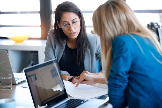 Photo shot of two business women working together with laptop in the office.