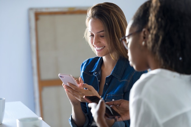 Scatto di due donne d'affari piuttosto giovani che usano i loro telefoni cellulari in ufficio.