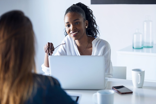 Scatto di due donne d'affari piuttosto giovani che lavorano con tablet digitale e laptop in ufficio.