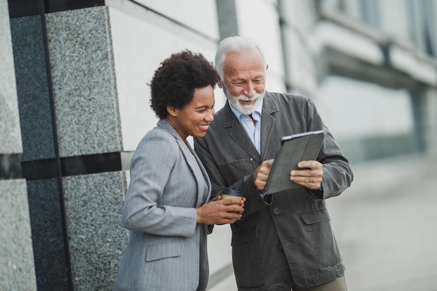 Shot of two successful multi-ethnic business people using digital tablet and having a discussion during a coffee break in front of the office building.