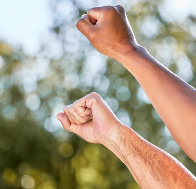 Photo shot of two unrecognisable men raising their fists in defiance outdoors