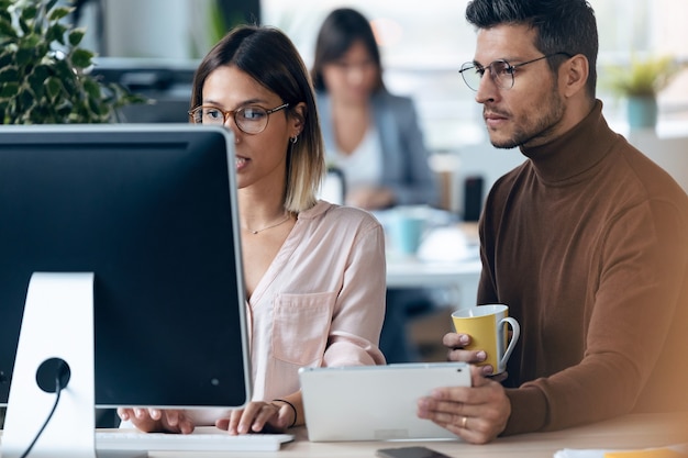 現代のワークスペースでコンピューターとデジタルタブレットを使用して作業している2人の若いビジネス同僚のショット。ブレーンストーミングの概念。