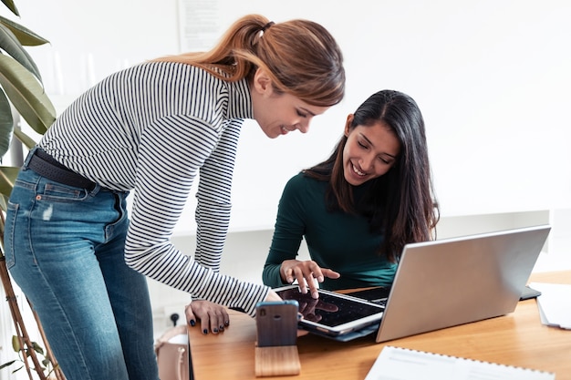 Inquadratura di due giovani imprenditrici che parlano e rivedono il loro ultimo lavoro sulla tavoletta digitale in ufficio.