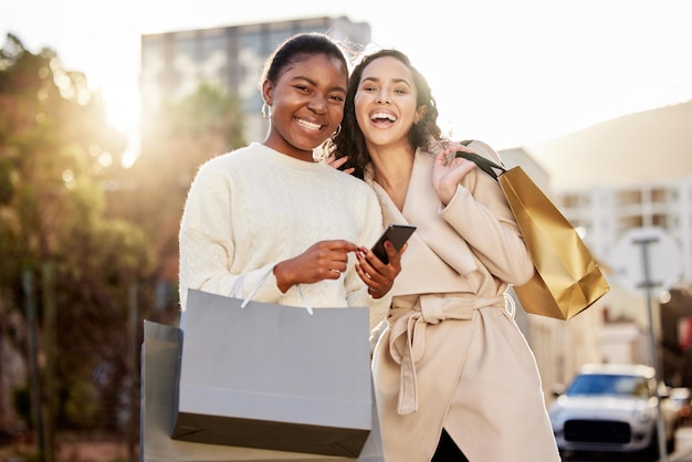 Photo shot of two young women using a smartphone while shopping against an urban background