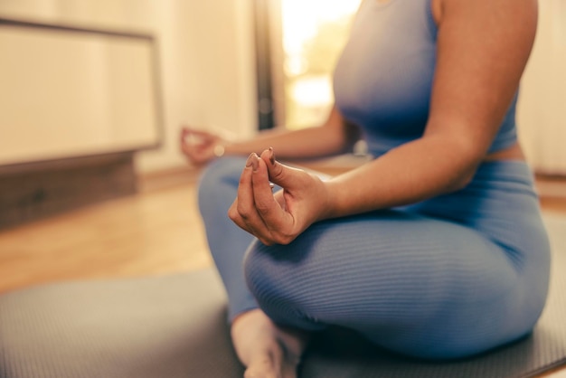 Shot of an unrecognisable woman meditating in the lotus position at home.