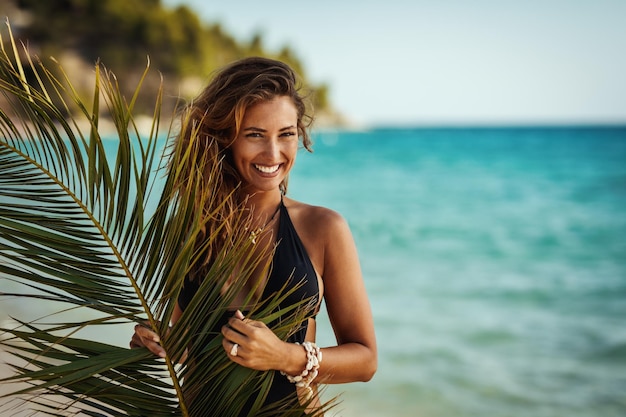 Shot van een aantrekkelijke jonge vrouw is poseren en genieten van bedekt met palmboomblad op het tropische strand.