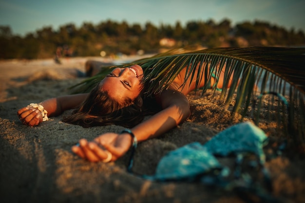 Shot van een aantrekkelijke jonge vrouw ligt op het tropische zandstrand bedekt met palmboomblad.