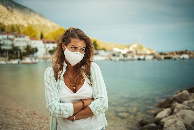 Shot van een bezorgde jonge vrouw met beschermend N95-masker op vakantie aan de kust tijdens de COVID-19.