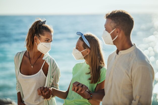 Shot van een gelukkig gezin met beschermend N95-masker dat tijd doorbrengt aan de kust tijdens de coronapandemie. Ze hebben van nature zelfisolatie.