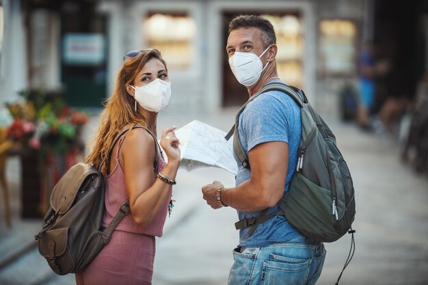 Shot van een gelukkig stel met beschermend N95-masker dat tijd doorbrengt op vakantie en een mediterrane stad verkent tijdens een coronapandemie.