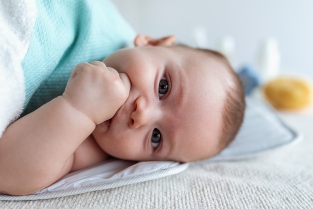 Shot van een gelukkige baby die naar de camera kijkt terwijl hij thuis op een wit vel ligt.