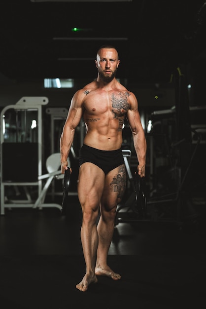 Shot van een gespierde bodybuilder die zijn perfecte spieren laat zien na het trainen met een gewichtsplaat in de sportschool.