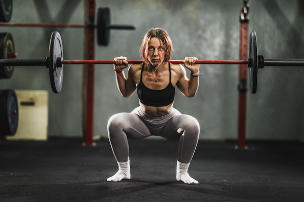 Shot van een gespierde jonge vrouw die traint op de harde training in de sportschool. Ze doet squat oefening met barbell.