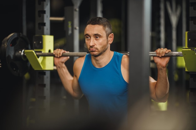 Shot van een gespierde man in sportkleding die traint in de cross-trainingsgymnastiek. Hij doet squat oefeningen met barbell.