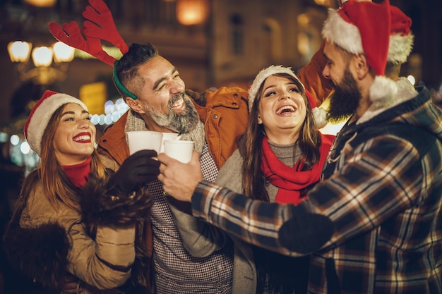 Shot van een groep vrolijke jonge vrienden die samen plezier hebben en genieten van glühwein op de kerstmarkt op een avondfeest.