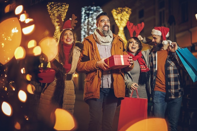 Shot van een groep vrolijke jonge vrienden met kerstcadeaus die plezier hebben tijdens een avondje uit.