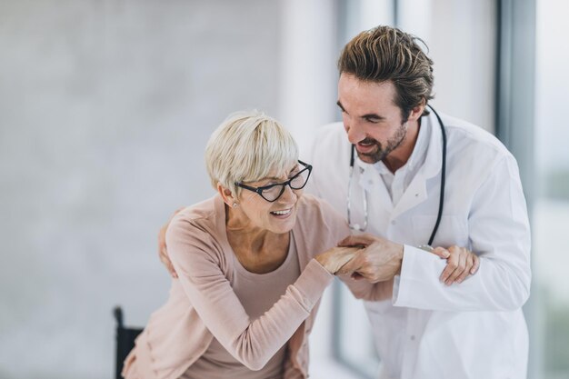 Shot van een jonge dokter die een oudere vrouw in een rolstoel helpt in de gang van het ziekenhuis.