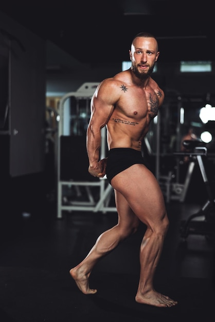 Shot van een jonge gespierde bodybuilder die zijn perfecte spieren laat zien terwijl hij poseert na het sporten in de sportschool.