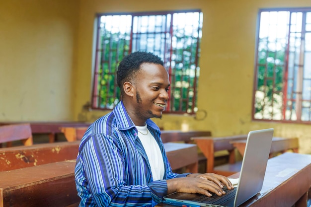 Shot van een jonge knappe Afrikaanse zwarte mannelijke student die typt en naar het scherm van een laptop kijkt