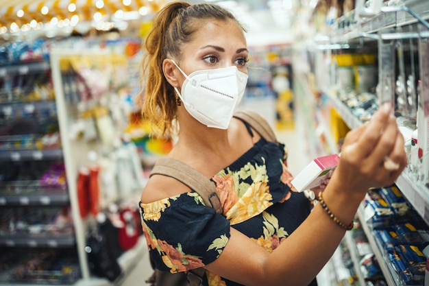 Shot van een jonge vrouw die een N95 beschermend masker draagt terwijl ze een supermarkt koopt tijdens de Covid-19-pandemie.