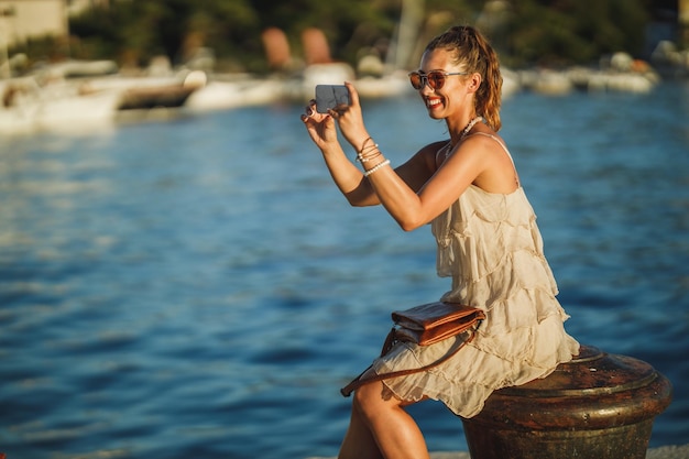 Shot van een jonge vrouw die foto's maakt met haar smartphone terwijl ze de prachtige kust van de Middellandse Zee verkent.