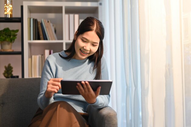 Shot van een jonge vrouw die haar digitale tablet gebruikt terwijl ze thuis op de bank zit