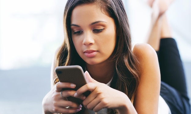 Shot van een jonge vrouw die op de grond ligt en een smartphone gebruikt