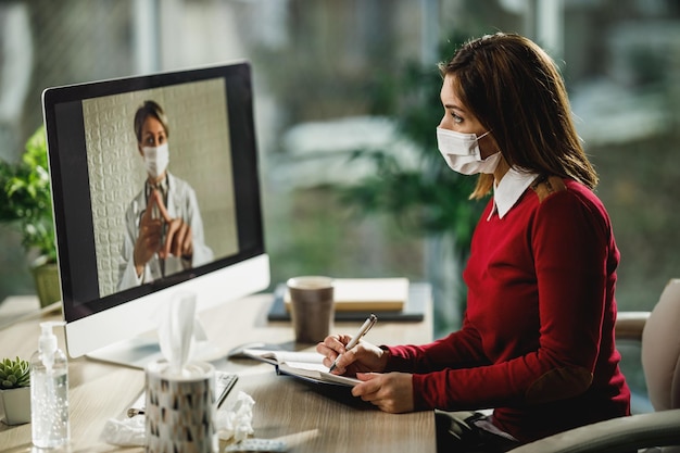 Shot van een jonge vrouwelijke patiënt die notities schrijft tijdens een videogesprek met haar arts op een computer.