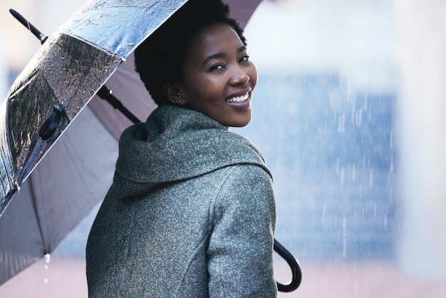 Shot van een jonge zakenvrouw die een paraplu gebruikt om zich mee te bedekken tijdens een wandeling in de regen tegen een stedelijke achtergrond