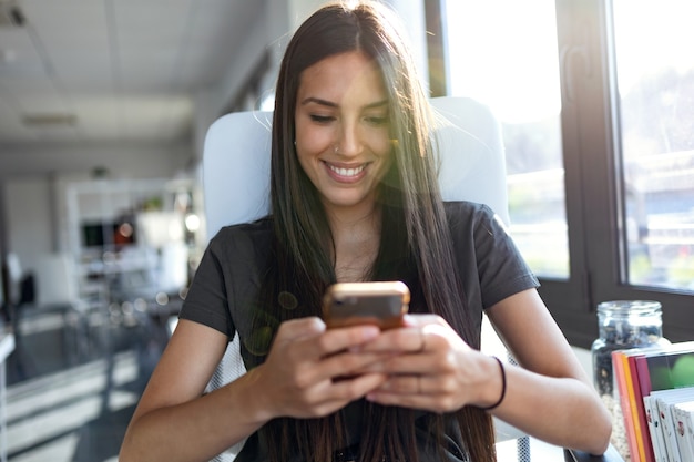 Shot van een lachende jonge zakenvrouw die berichten verzendt met een mobiele telefoon terwijl ze op kantoor zit.