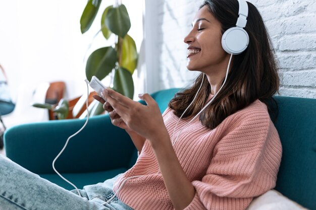 Shot van een mooie jonge vrouw die naar muziek luistert met een digitale tablet terwijl ze thuis op de bank zit.