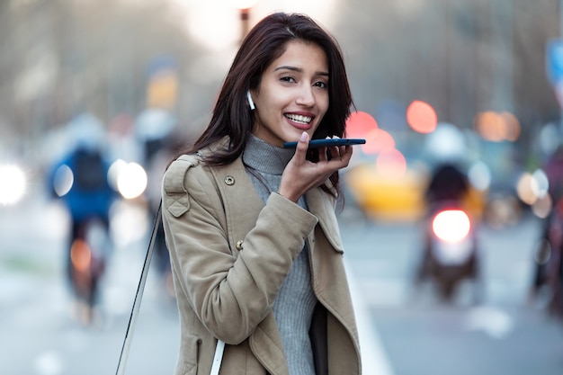 Shot van een mooie jonge vrouw die spraakherkenningssysteem op haar smartphone gebruikt terwijl ze op straat staat.