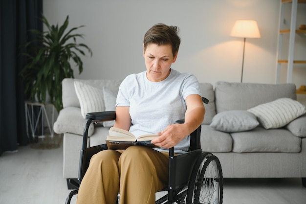 Shot van een oudere vrouw die in een rolstoel zit en thuis een boek leest