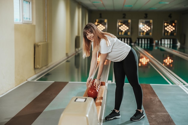 Shot van een schattige jonge vrouw met een bowlingbal in de bowlingclub.