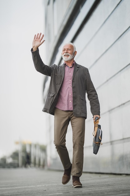 Shot van een succesvolle senior zakenman begroet iemand terwijl hij door een straat loopt, voor een bedrijfsgebouw.