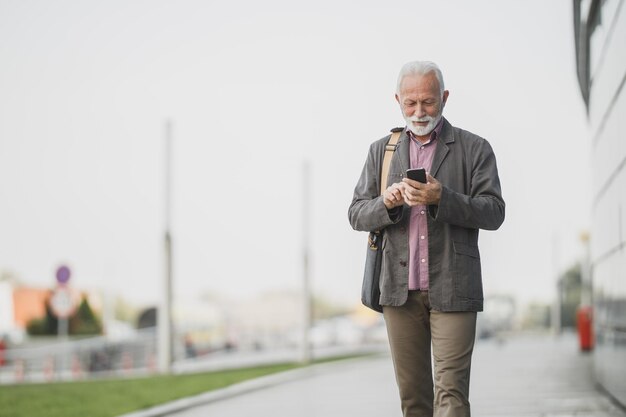 Shot van een succesvolle senior zakenman die sms't op een smartphone terwijl hij door een straat loopt, voor een bedrijfsgebouw.