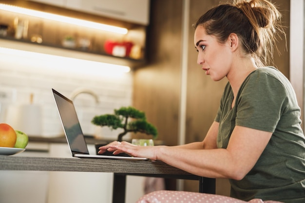 Shot van een vrouw die haar laptop 's ochtends in haar keuken thuis gebruikt.