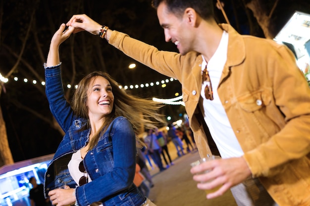 Shot van een zorgeloos jong stel dat 's nachts hand in hand danst in de eetmarkt op straat.