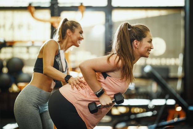 Shot van een zwangere vrouw die traint met een halter onder controle van de vrouwelijke personal trainer in de sportschool.