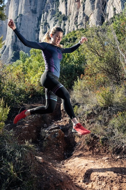 Shot van jonge fitness vrouw trail runner rennen en springen op rotsachtige berg.