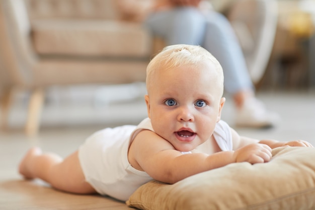 shot van speelse baby plezier op vloer liggend op kussen terwijl zijn moeder zittend op de bank