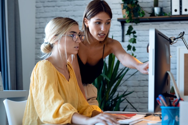 Shot van twee mooie freelance zakelijke vrouwenverkopers die de productbestelling controleren met de computer in hun startende kleine onderneming.