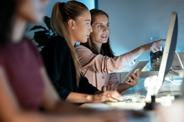 Shot van twee slimme zakenvrouwen die samenwerken met computer en digitale tablet terwijl ze op kantoor praten.