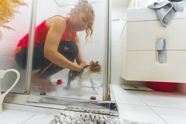 Shot vanuit een gemiddeld perspectief van een vrouw in een rood topje die een kat aan het douchen is in een badkamerdouche, genomen vanaf de zijkant